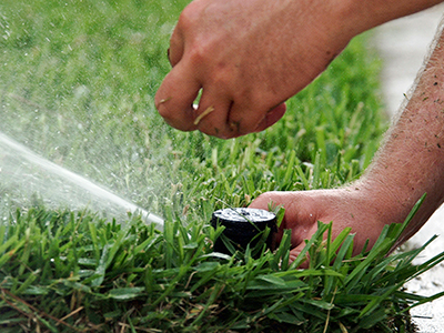 close up of hands adjusting a sprinkler head so it points towards grass and not the sidewalk