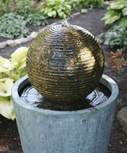 A fountain with a concrete sphere with water spilling over it into a pedestal