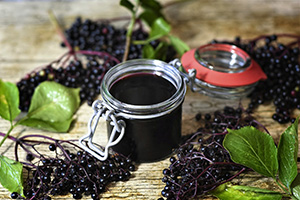 small canning jar of deep purple jelly almost black surrounded by clusters of tiny tiny-purple elderberry fruits