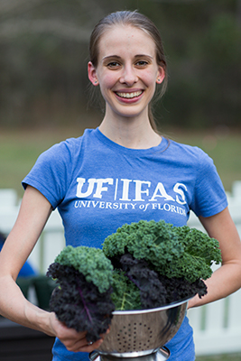 Woman wearing UF/IFAS shirt and holding freshly harvested kale