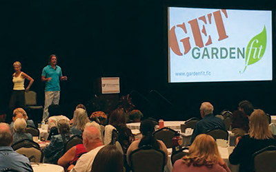 Two fitness instructors present on stage at the conference, the big screen showing the presentation title Get Garden Fit
